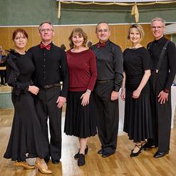 Sechs Tanzpaare stehen in eleganter Kleidung, vor einem Spiegel und einer Tanzfl&auml;che in einem hellen Saal.