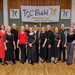 Gruppenfoto von T&auml;nzern in eleganter Kleidung vor dem Banner des TSC Br&uuml;hl im Tanzen.