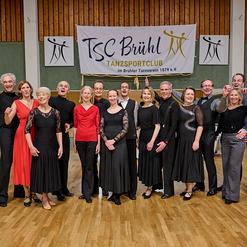 Gruppenfoto von T&auml;nzern in eleganter Kleidung vor einem Banner des TSC Br&uuml;hl im Tanzsportclub.