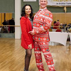 Ein Paar posiert auf einer Tanzfl&auml;che; der Mann tr&auml;gt einen festlichen roten Anzug mit Weihnachtsmotiven, die Frau ein rotes Outfit.