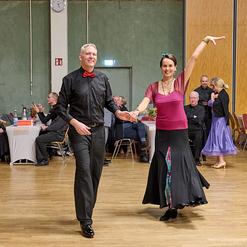 Tanzendes Paar in eleganter Kleidung auf der Tanzfl&auml;che, umgeben von G&auml;sten in einem festlichen Saal.