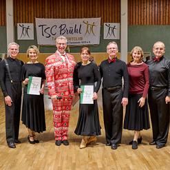 Gruppe von T&auml;nzern in formeller Kleidung, die Preistr&auml;ger mit Urkunden in einer Tanzhalle des TSC Br&uuml;hl sind.