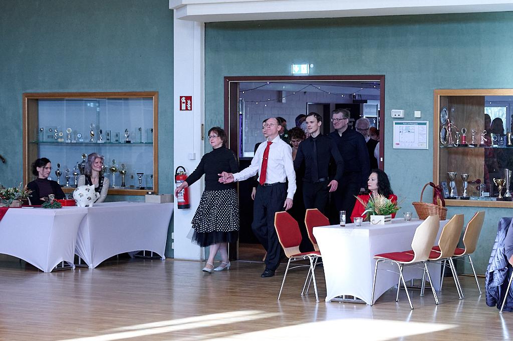 Menschen betreten einen festlich geschm&uuml;ckten Raum, w&auml;hrend mehrere G&auml;ste an Tischen sitzen und zuschauen.