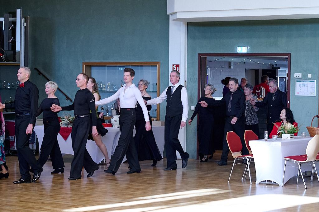 Tanzende Paare in eleganter Abendkleidung bewegen sich durch einen festlich dekorierten Raum.
