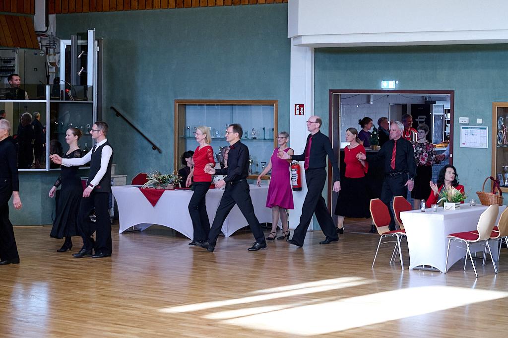 Tanzende Paare in formeller Kleidung bewegen sich durch einen festlich dekorierten Festraum.