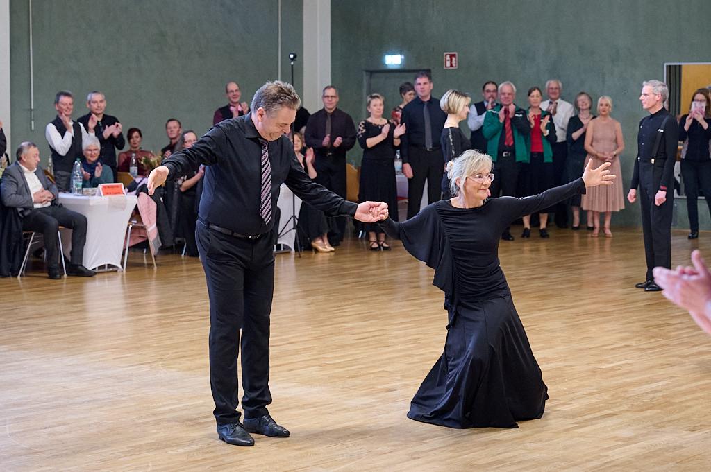 Tanzpaar in festlicher Kleidung pr&auml;sentiert eine Darbietung vor applaudierender Menge in einem Veranstaltungsraum.