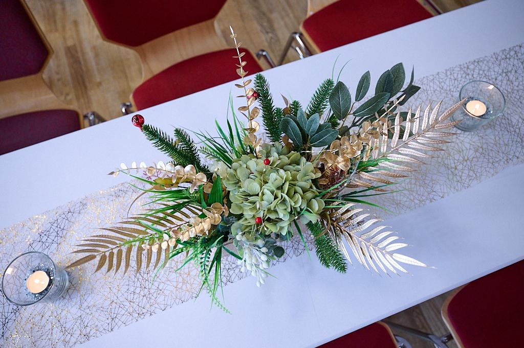 Dekoratives Tischarrangement mit gr&uuml;nen Pflanzen, goldenen Akzenten und Kerzen auf einem wei&szlig;en Tisch.