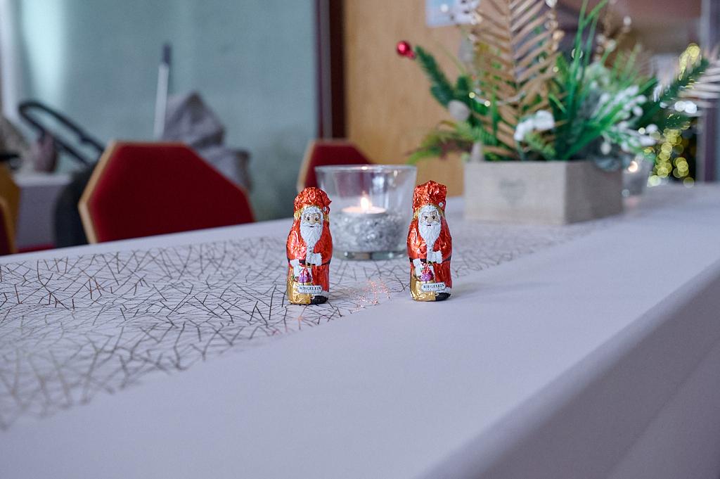 Zwei Schokoladen-Weihnachtsm&auml;nner stehen auf einem festlich gedeckten Tisch mit einer Kerze und gr&uuml;nem Dekor.