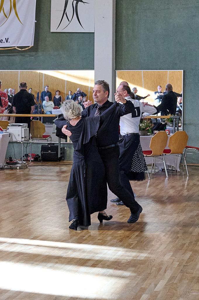 Zwei Paare tanzen in eleganter Kleidung auf einer Tanzfl&auml;che, im Hintergrund Zuschauer und festliche Dekoration.