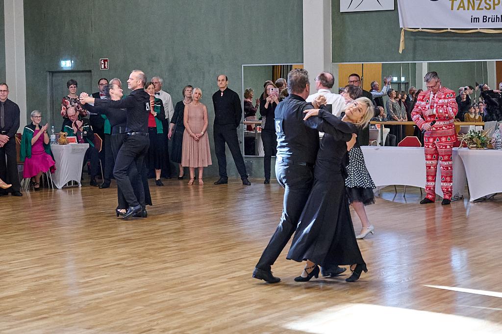 Tanzende Paare in eleganter Kleidung auf einer Tanzfl&auml;che, umgeben von applaudierenden Zuschauern bei einer Veranstaltung.