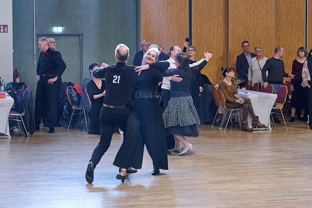 Tanzpaar in eleganter Kleidung auf einer Veranstaltung, umgeben von Zuschauern, die applaudieren und zuschauen.