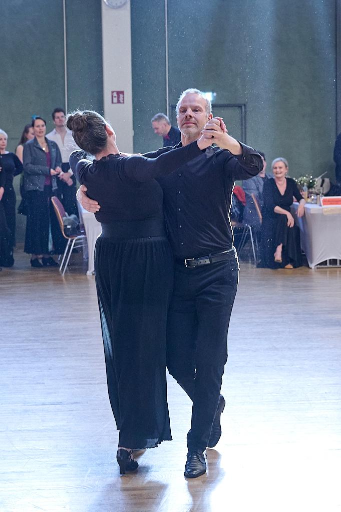 Tanzpaar in eleganter Kleidung tanzt in einer festlichen Umgebung, im Hintergrund Zuschauer auf einer Tanzveranstaltung.