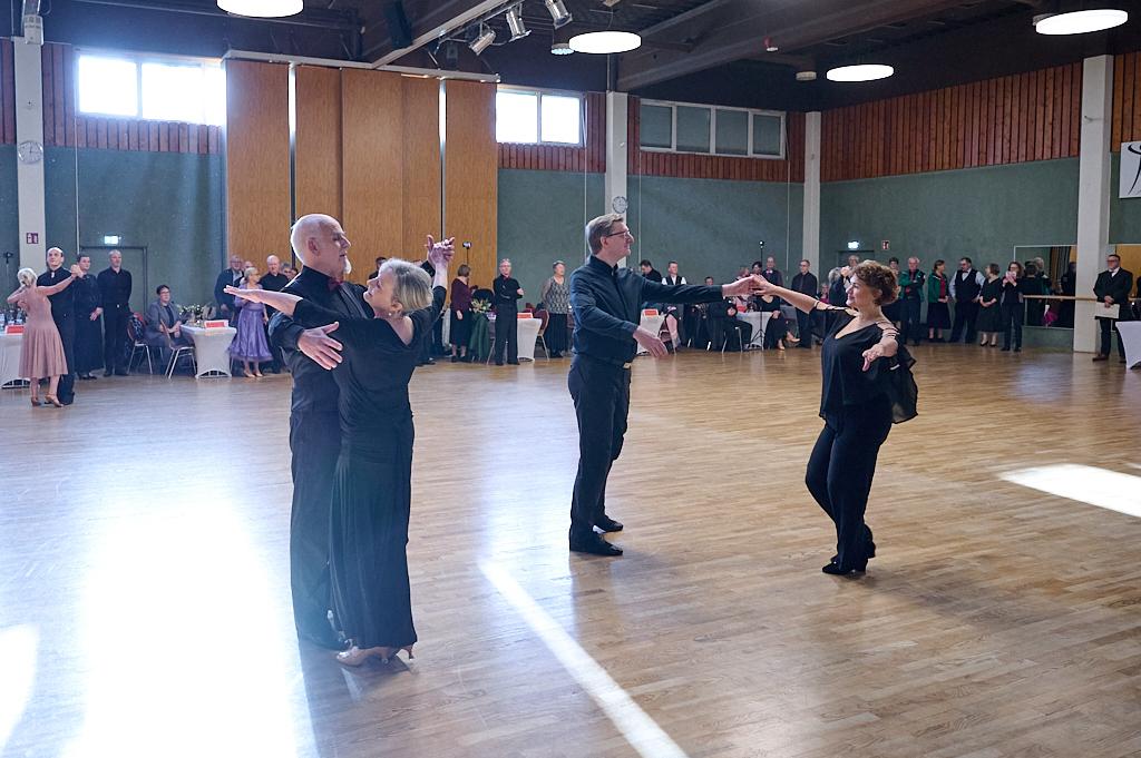 Tanzende Paare in eleganter Kleidung auf einer Tanzfl&auml;che, umgeben von Zuschauern in einem Veranstaltungssaal.