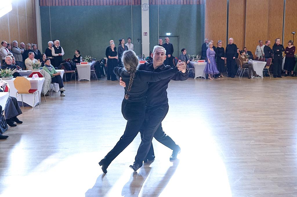 Tanzendes Paar in blauen Outfits auf einer Tanzfl&auml;che, umgeben von Publikum in einem festlichen Saal.