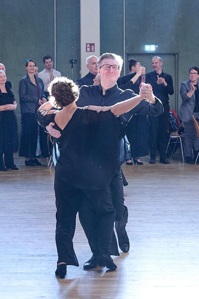 Tanzpaar in eleganter Kleidung w&auml;hrend eines Tanzwettbewerbs, umgeben von applaudierendem Publikum.