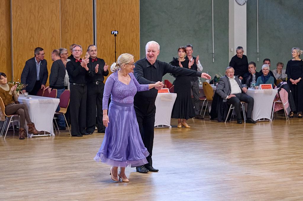 Tanzpaar in eleganter Kleidung bei einem Tanzabend, umgeben von applaudierendem Publikum in einem festlichen Saal.