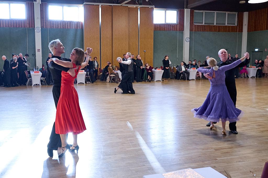 Tanzveranstaltung in einem Saal mit Paaren in eleganter Tanzkleidung auf Holzfu&szlig;boden.
