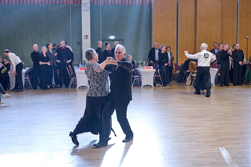 Tanzendes Paar in eleganter Kleidung auf einer Tanzfl&auml;che, umgeben von Zuschauern in einem festlichen Ambiente.