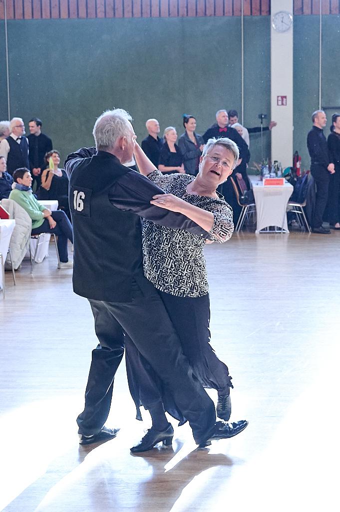 Tanzendes Paar in eleganter Kleidung auf einer Tanzveranstaltung, mit Zuschauern im Hintergrund.