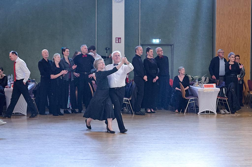 Tanzpaar in eleganter Kleidung auf einer Tanzfl&auml;che, umgeben von Zuschauern in festlicher Atmosph&auml;re.