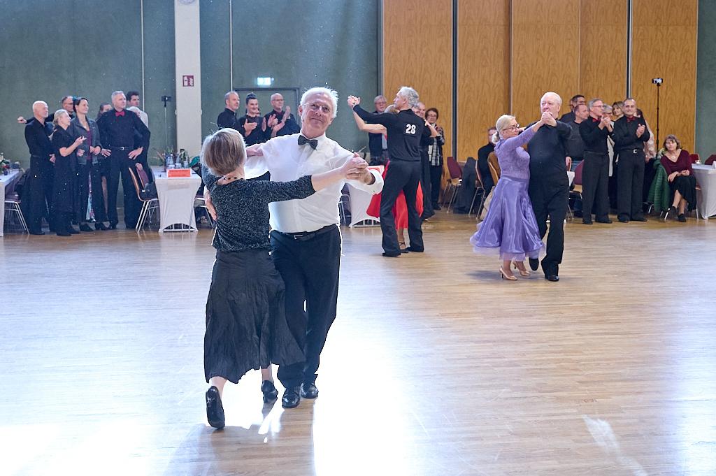 Tanzpaare pr&auml;sentieren sich auf einer Fl&auml;che, umgeben von Zuschauern in einem festlichen Saal.