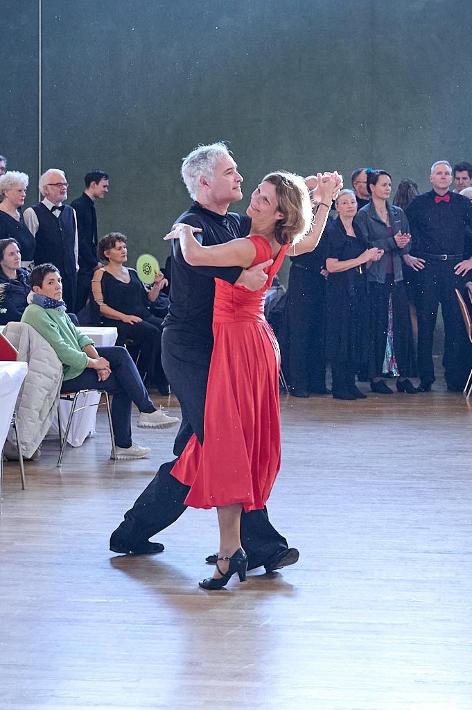Tanzendes Paar in eleganter Kleidung, umgeben von Zuschauern in einem festlichen Saal.