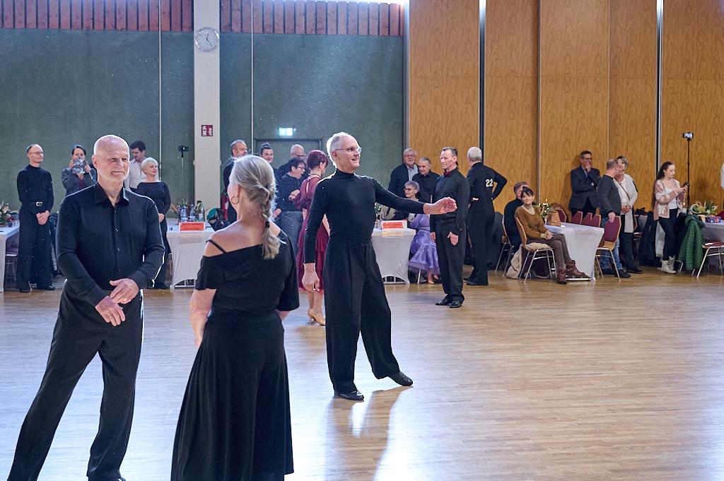 Tanzpaare in eleganter Kleidung auf einer Tanzfl&auml;che, im Hintergrund Zuschauer an Tischen.