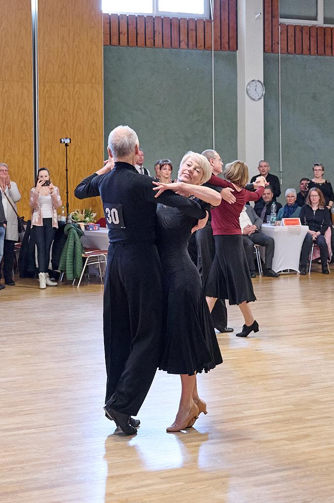 Tanzpaar in eleganter Kleidung tanzt auf einer Veranstaltung, Zuschauer im Hintergrund applaudieren.