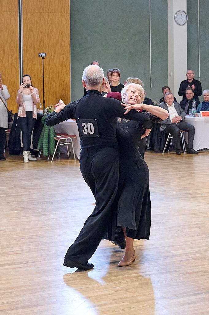Tanzendes Paar in eleganter Kleidung auf einer Tanzfl&auml;che, umgeben von Zuschauern in einem Festsaal.