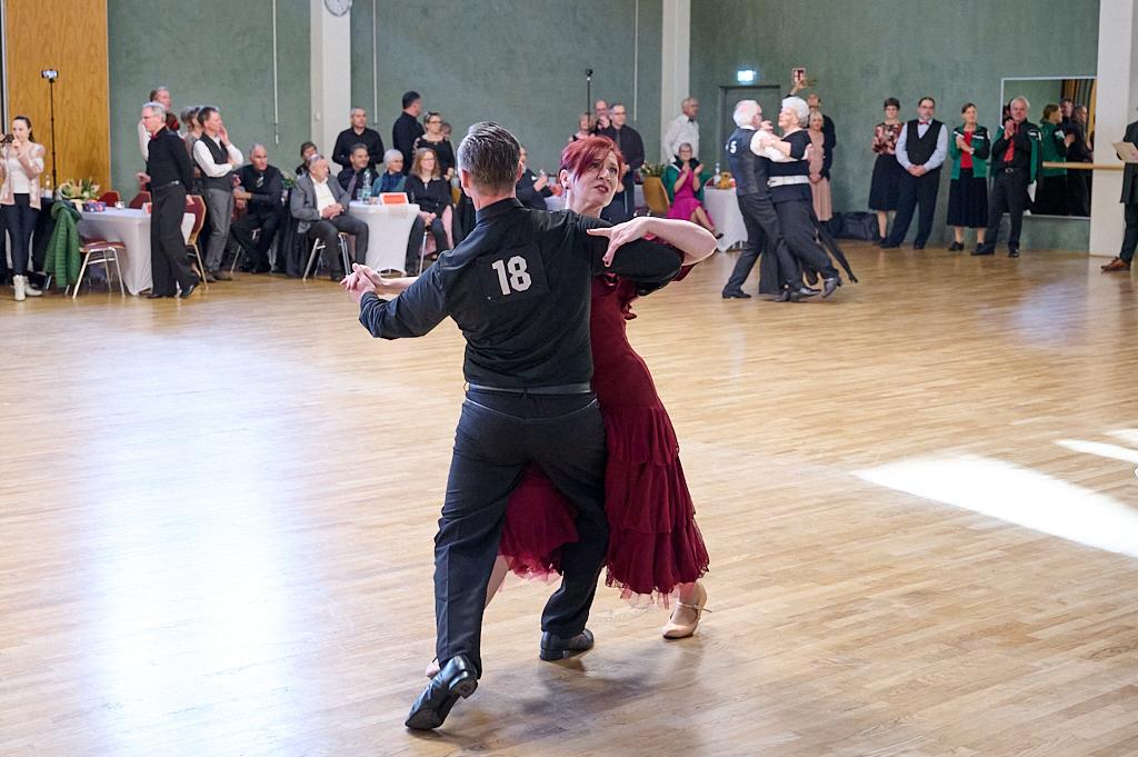 Tanzpaar in Bewegung auf einer Tanzfl&auml;che, umgeben von Zuschauern in einem festlichen Saal.