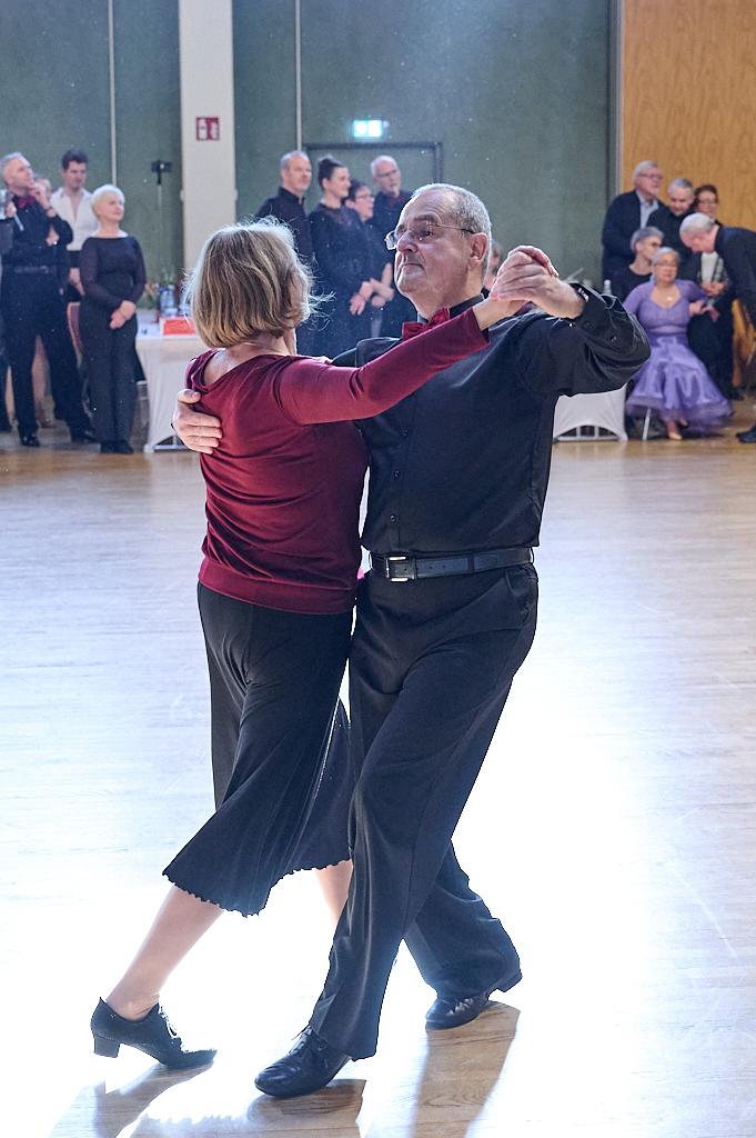 Tanzpaar in eleganter Kleidung, das in einem Festsaal miteinander tanzt, umgeben von begeistertem Publikum.