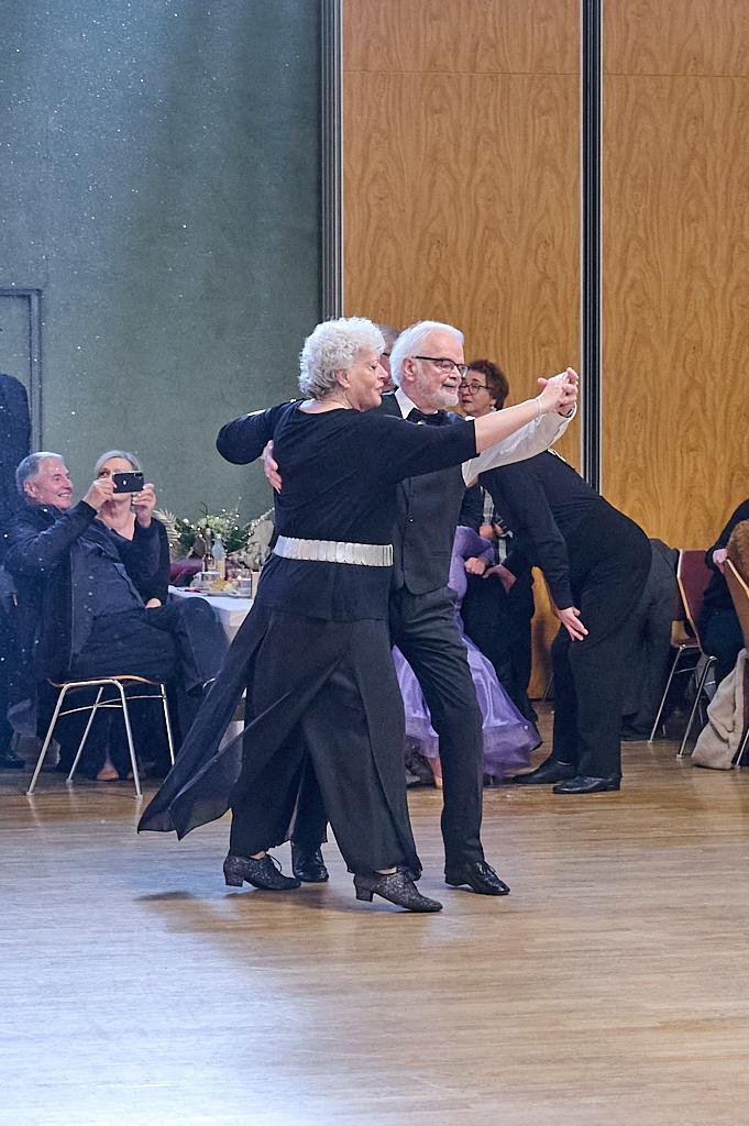 Tanzendes Paar in eleganter Kleidung auf einer Tanzfl&auml;che, mit anderen G&auml;sten im Hintergrund, die zuschauen.