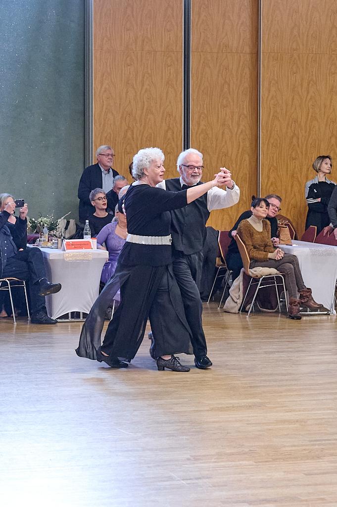 Tanzendes Paar in eleganter Kleidung auf einer Tanzfl&auml;che, Zuschauer beobachten in einem festlichen Saal.