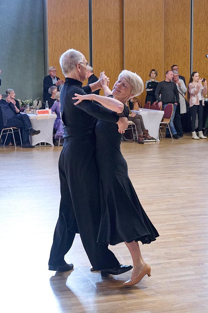 Tanzendes Paar in eleganter Kleidung auf einer Tanzfl&auml;che, umgeben von Zuschauern in einem festlichen Saal.