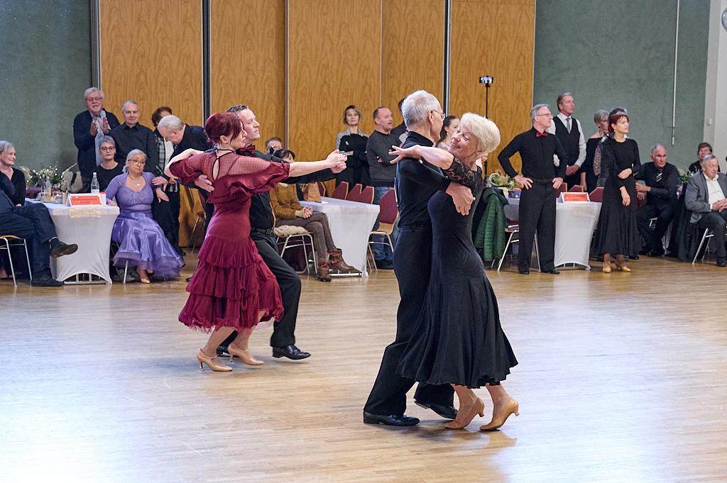 Tanzende Paare in eleganter Kleidung auf einer Holzfl&auml;che, umgeben von applaudierenden Zuschauern.