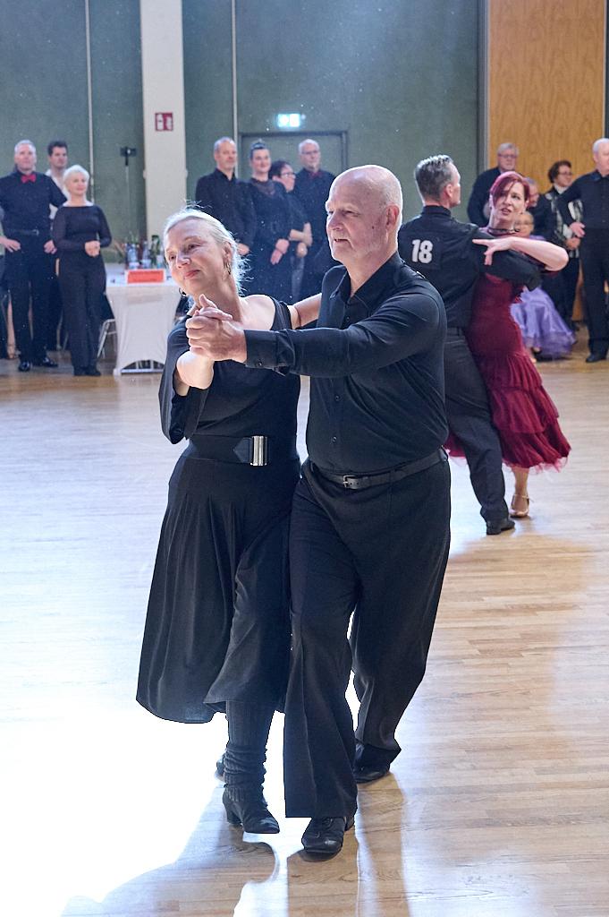 Tanzendes Paar in eleganter Kleidung auf einer Tanzfl&auml;che, umgeben von weiteren T&auml;nzern und Zuschauern.