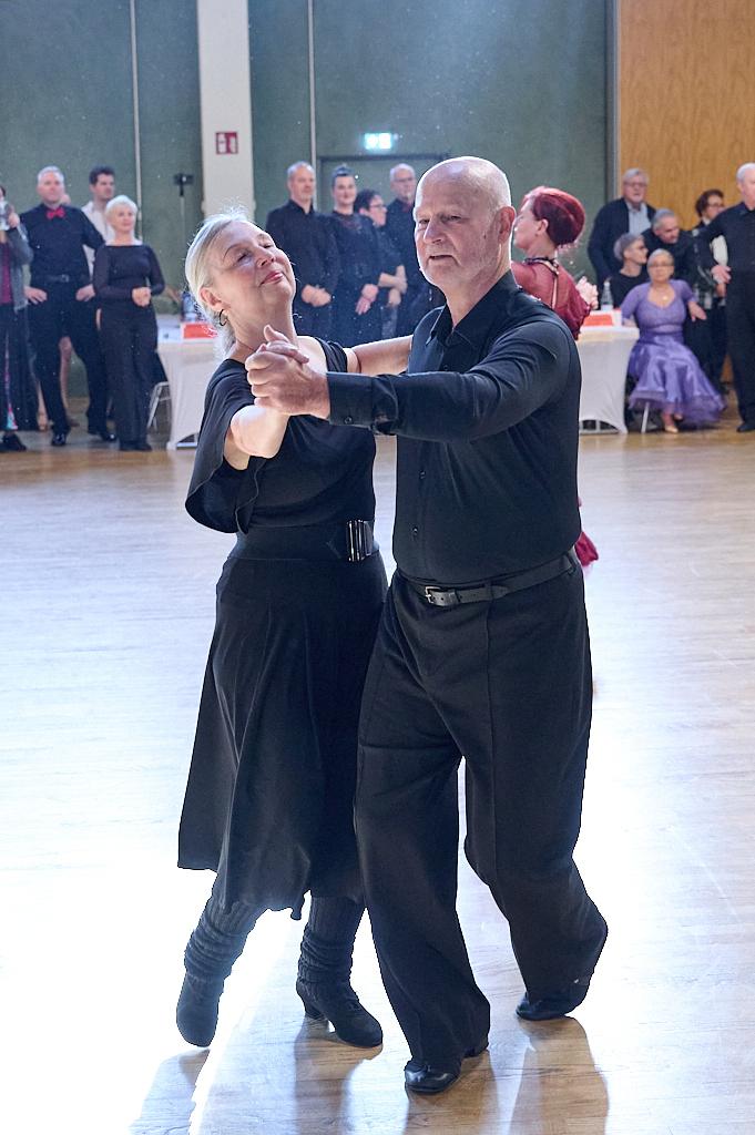 Tanzendes Paar in schwarzer Kleidung auf einer Tanzfl&auml;che, umgeben von einer Zuschauermenge.