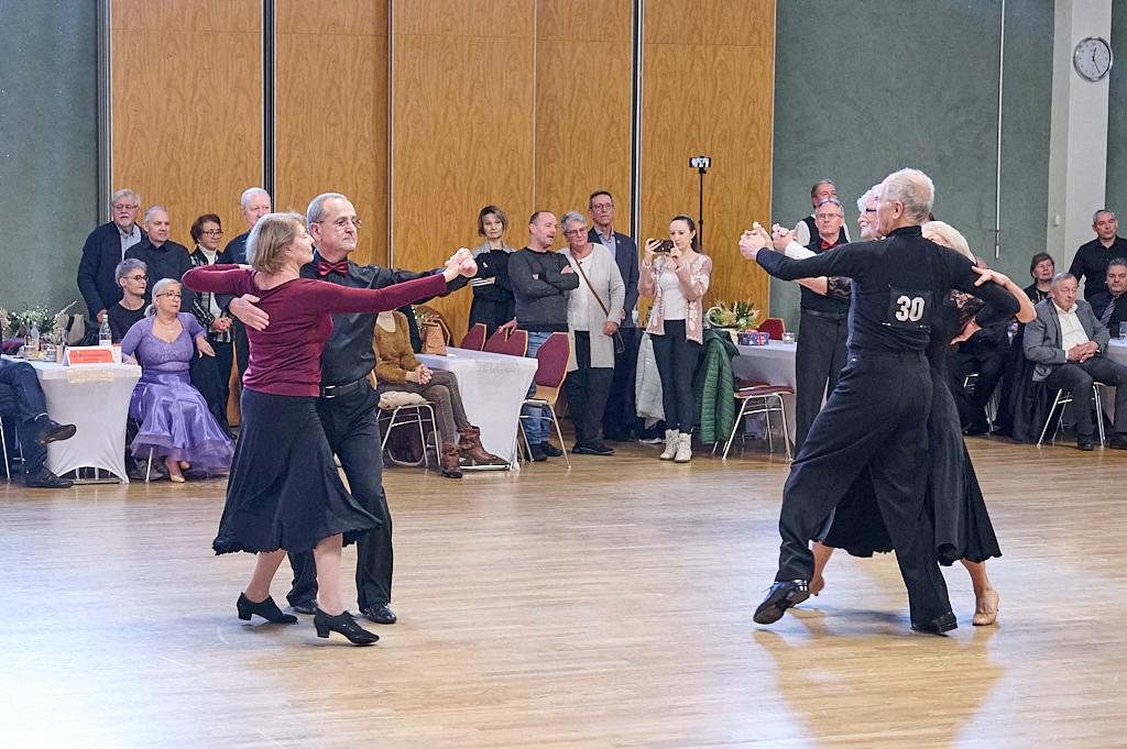 Zwei Paare tanzen in eleganter Kleidung auf einer Tanzfl&auml;che, w&auml;hrend eine Zuschauergruppe beobachtet.