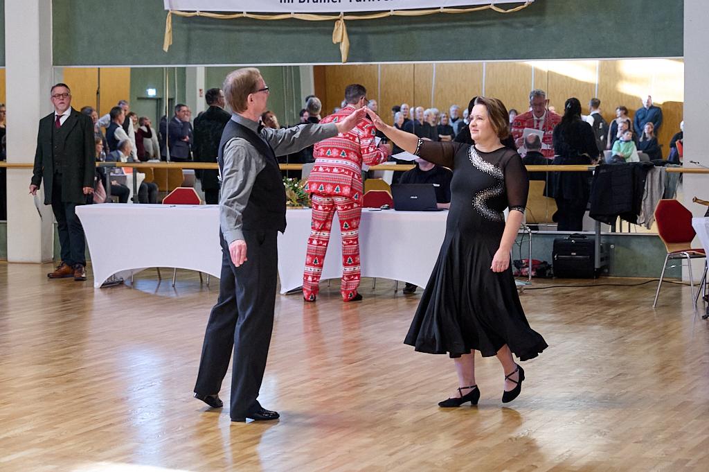 Tanzpaar f&uuml;hrt einen langsamen Walzer auf einer Tanzfl&auml;che, Zuschauer im Hintergrund, festliche Stimmung im Saal.