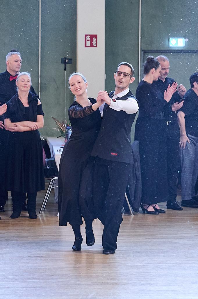Tanzendes Paar in eleganter Kleidung auf einer Tanzfl&auml;che, umgeben von applaudierenden Zuschauern.