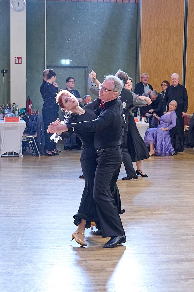 Tanzpaar in eleganter Kleidung f&uuml;hrt einen Tanzschritt auf einer Holztanzfl&auml;che w&auml;hrend einer Veranstaltung.