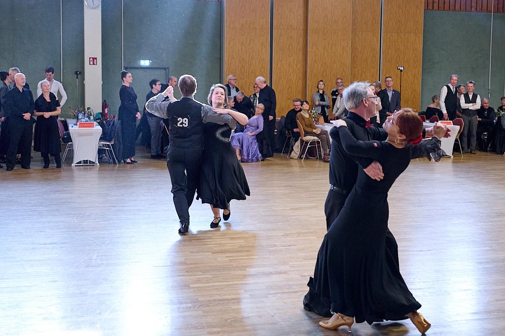 Tanzenden Paare in eleganten Kleidern auf einer Holz-Tanzfl&auml;che w&auml;hrend einer Tanzveranstaltung im Hintergrund.