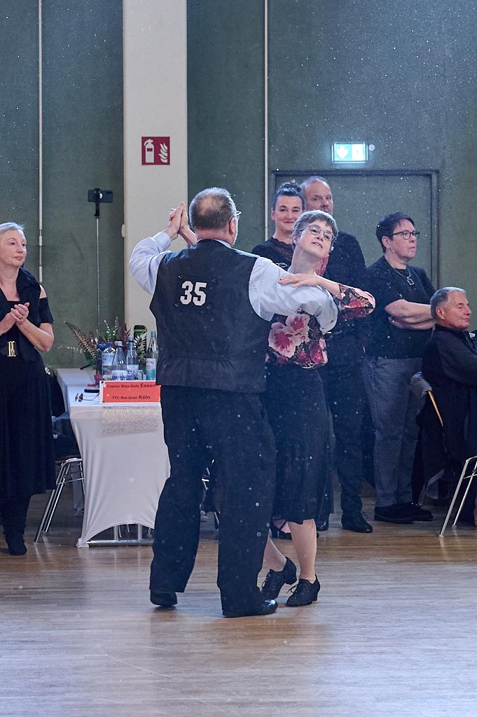 Tanzpaar in eleganter Kleidung beim Tanzen, umgeben von applaudierendem Publikum in einer festlichen Halle.