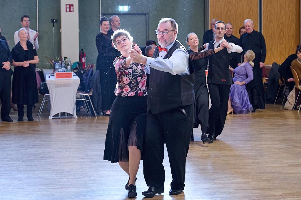 Tanzpaar in eleganter Kleidung vollf&uuml;hrt einen Langsame-Walzer in einem festlichen Saal mit Publikum im Hintergrund.
