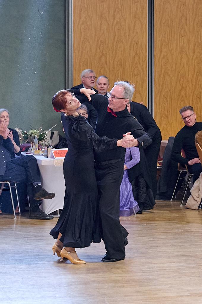 Tanzpaar in eleganter Kleidung f&uuml;hrt einen Tango auf einer Tanzfl&auml;che, Zuschauer applaudieren im Hintergrund.