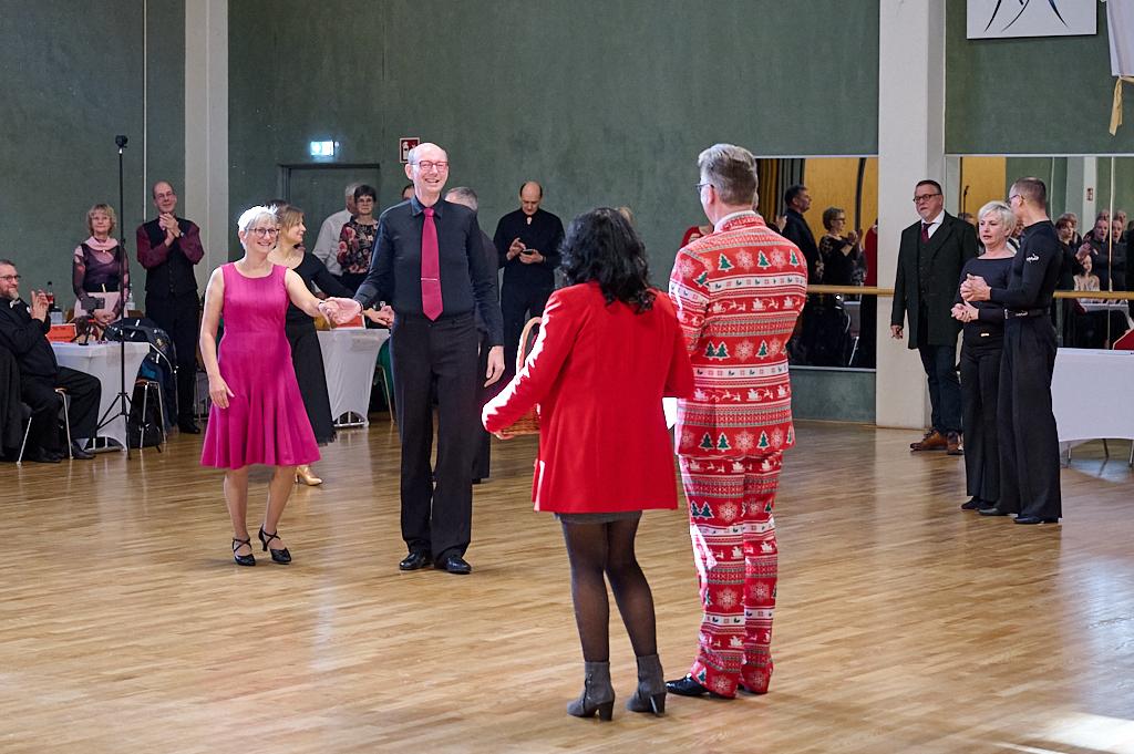Tanzveranstaltung in einem Saal mit mehreren Teilnehmern, die in festlicher Kleidung miteinander tanzen.