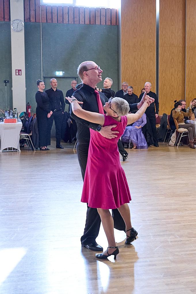 Tanzendes Paar in eleganter Kleidung auf einer Tanzfl&auml;che, umgeben von Zuschauerinnen und Zuschauern.