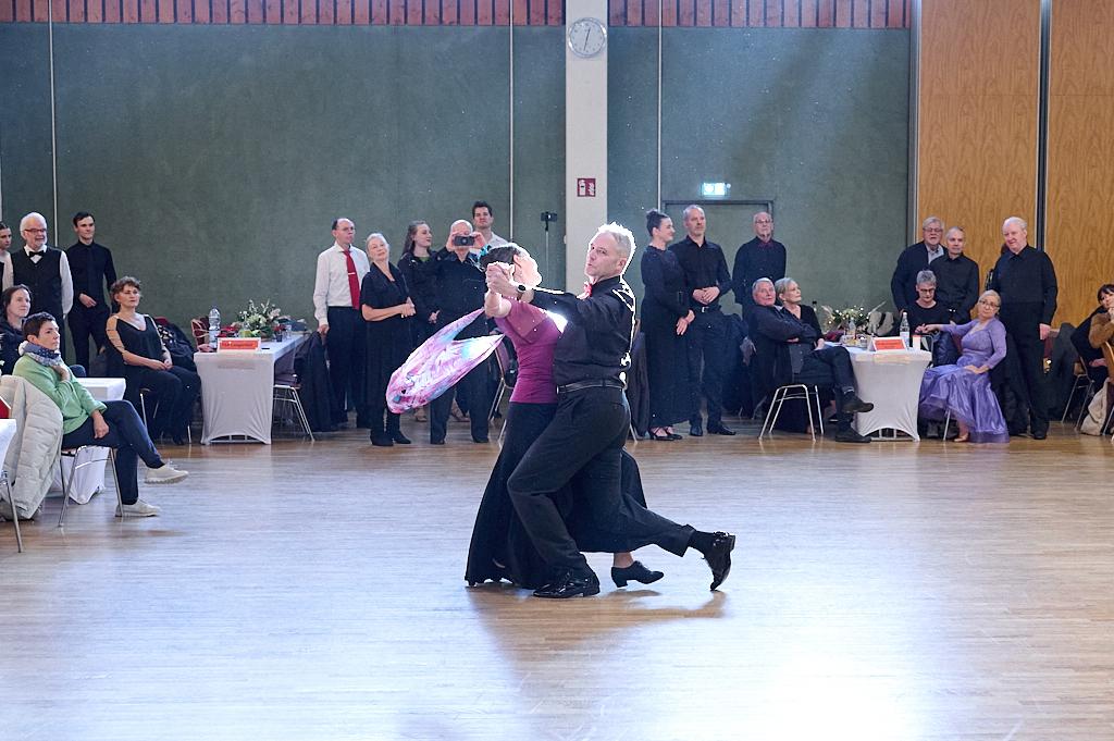 Tanzpaar in eleganter Pose auf der Tanzfl&auml;che, Zuschauer in Abendkleidung sitzen an Tischen im Hintergrund.