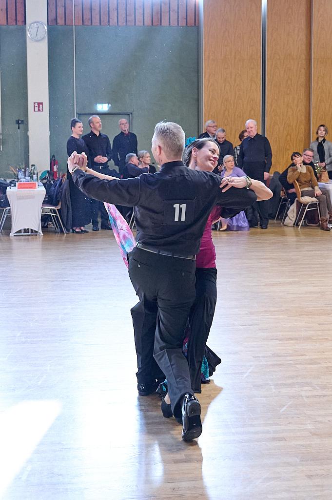 Tanzendes Paar in eleganter Kleidung, umgeben von Zuschauern in einem festlichen Saal.