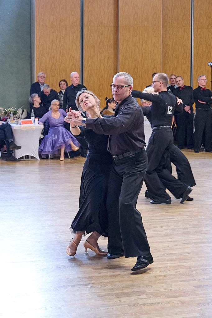 Tanzpaar f&uuml;hrt einen engagierten Tango auf einer Tanzfl&auml;che, Zuschauer beobachten im Hintergrund.